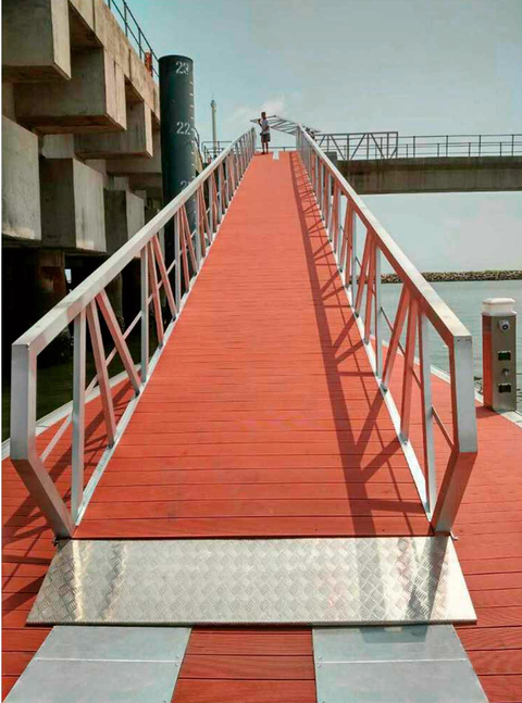 Pasarela de acceso con piso rojo y barandales de aluminio en un puerto